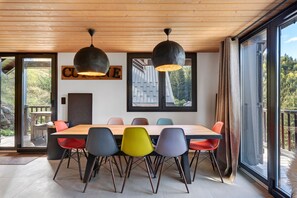 A modern dining area with a wooden table and colorful chairs, a sign reading 'CULTURE', and large windows offering a view of the outdoors.
