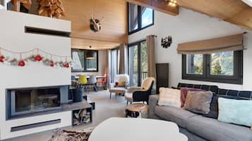 Un interior moderno con chimenea, un sofá, un comedor y ventanas grandes con vistas al exterior.