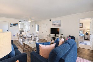 A spacious living area with a sofa, TV, and dining table. - Ocean-View North Beach Condo with Pools & Community Private Beach Access (Tybee Island)