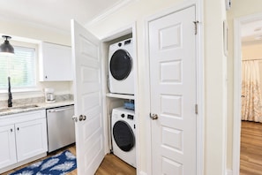 A laundry room with two stacked washing machines, a coffee maker on the counter, and a blue rug on the floor. - Ocean-View North Beach Condo with Pools & Community Private Beach Access (Tybee Island)