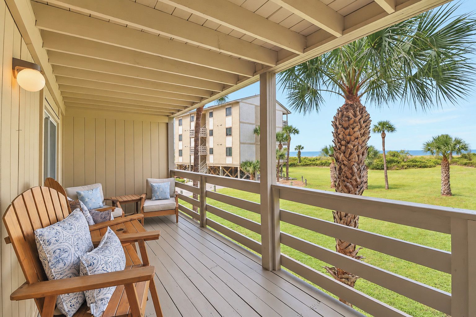 A covered outdoor area with wooden furniture, a view of a building, and a palm tree.