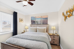 A bedroom with a bed, bedside lamps, a ceiling fan, and artwork on the wall. - Ocean-View North Beach Condo with Pools & Community Private Beach Access (Tybee Island)