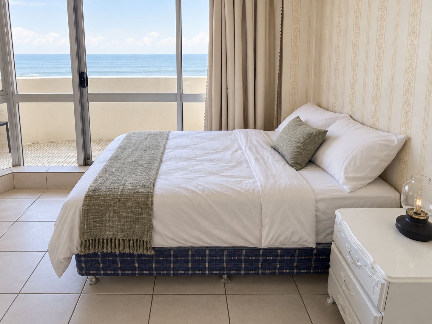 A bedroom with a bed, a nightstand, and a view of the beach.