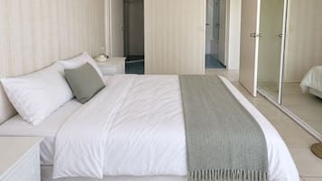 A neatly made bed with white linens and a grey throw, a bedside table with a lamp, and a large mirror on the wall.