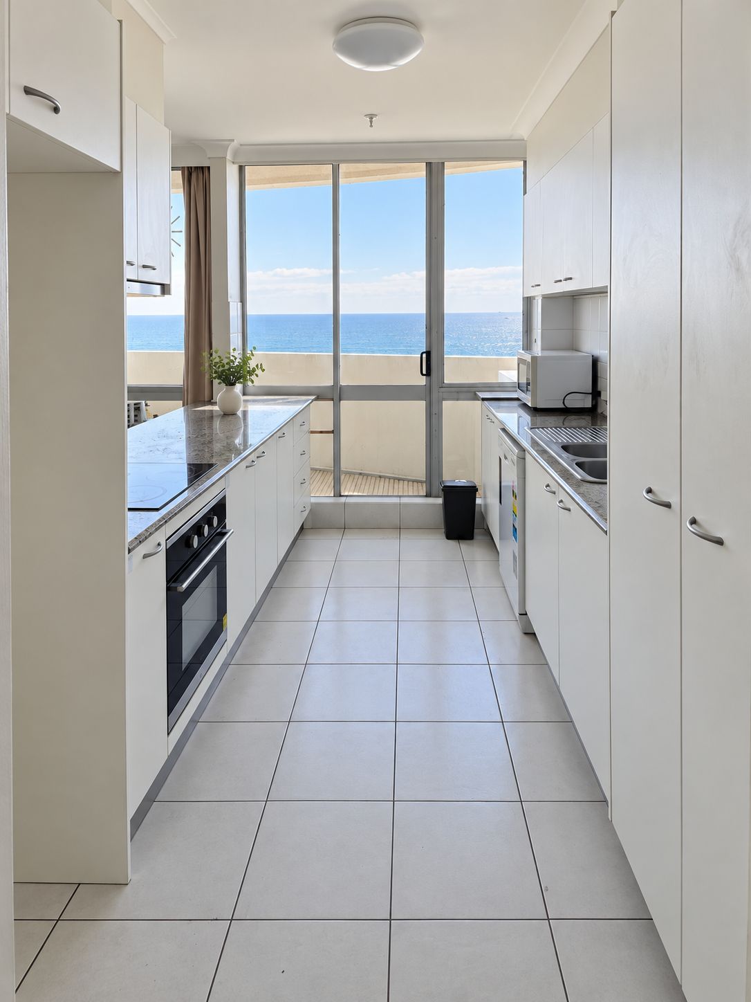 A modern kitchen with a view of the sea, featuring white cabinets, a stove, and a microwave.