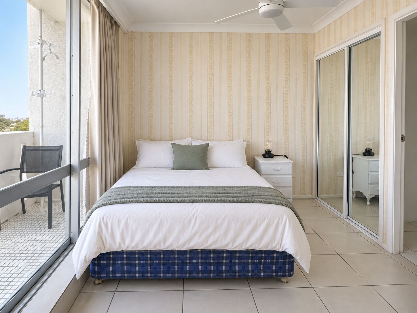 A bedroom with a bed, a nightstand, a chair, and a sliding glass door leading to a balcony.