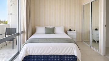 A bedroom with a bed, a nightstand, a chair, and a sliding glass door leading to a balcony.