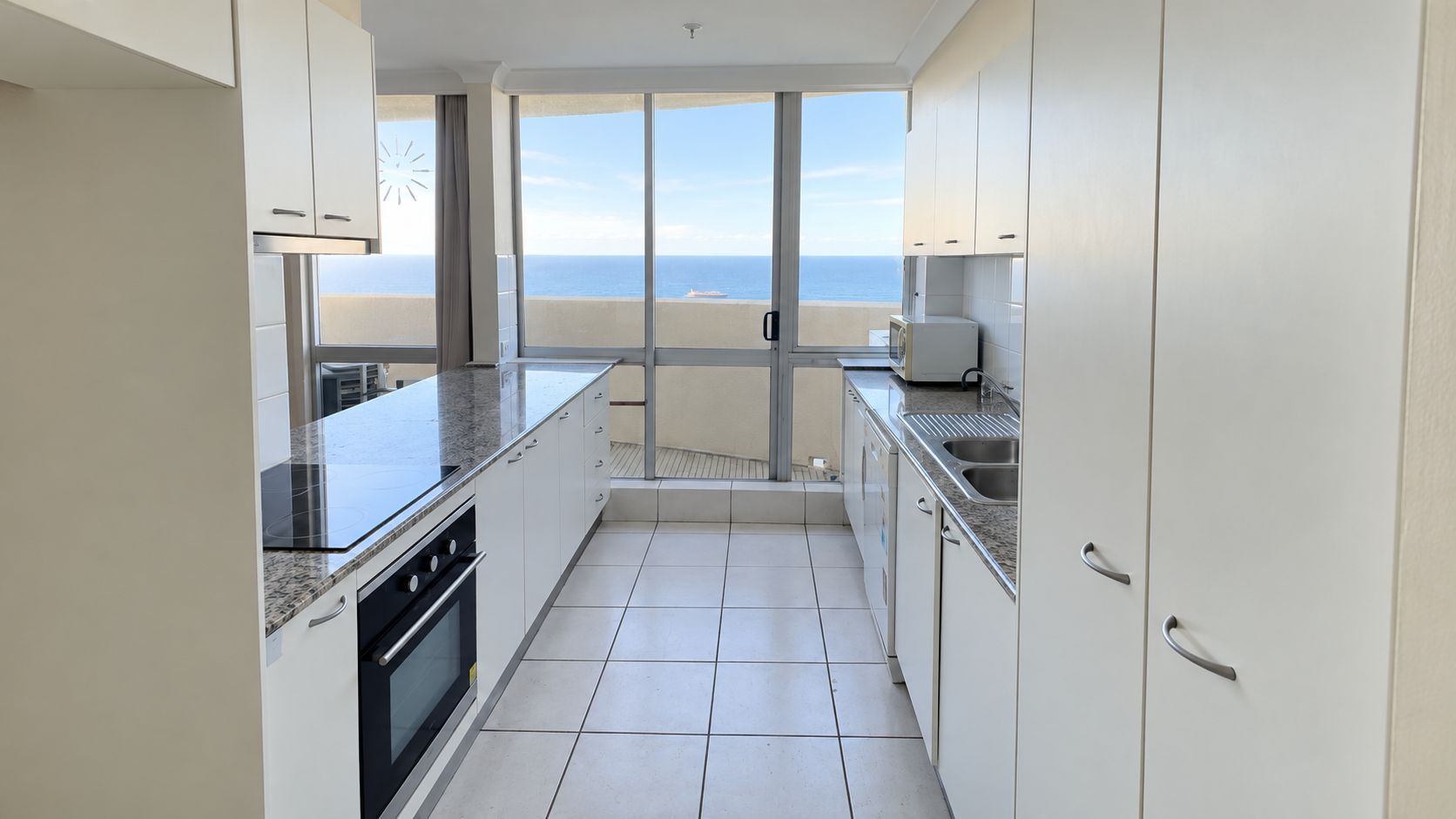A modern kitchen with a view of the sea, featuring white cabinets, a granite countertop, and a built-in oven.