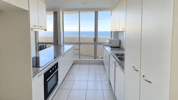 A modern kitchen with a view of the sea, featuring white cabinets, a granite countertop, and a built-in oven.