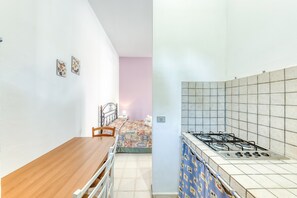 Una stanza con un tavolo da pranzo in legno, un letto con copriletto decorato e una kitchenette con piano cottura a gas.