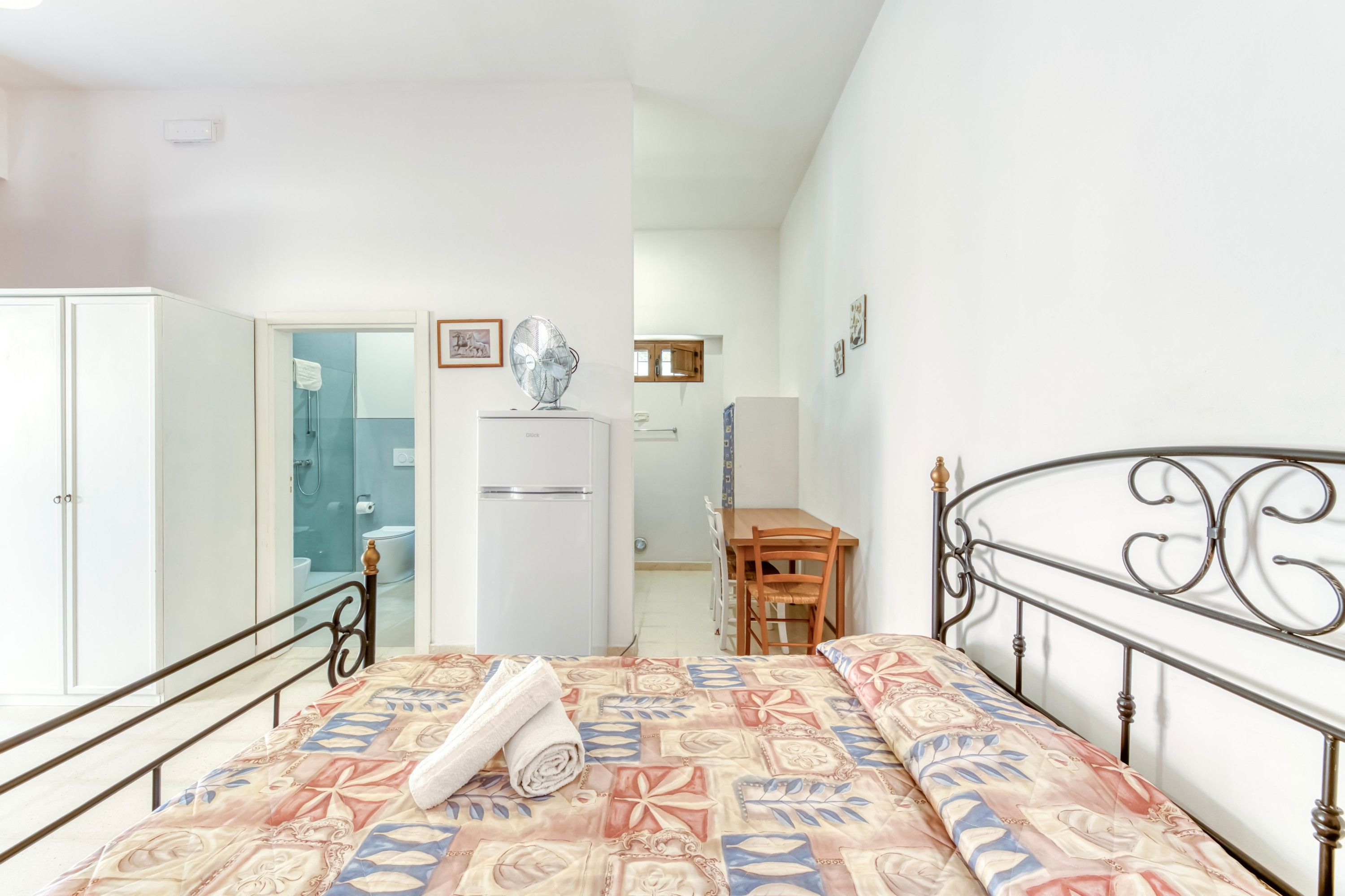 Una camera da letto con un letto, un armadio, una scrivania e un bagno visibile tramite una porta aperta.