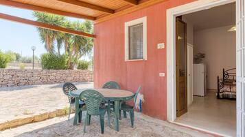 Un'area patio coperta con tavolo e sedie, un muro in pietra e una porta che dà su una camera da letto con un letto.