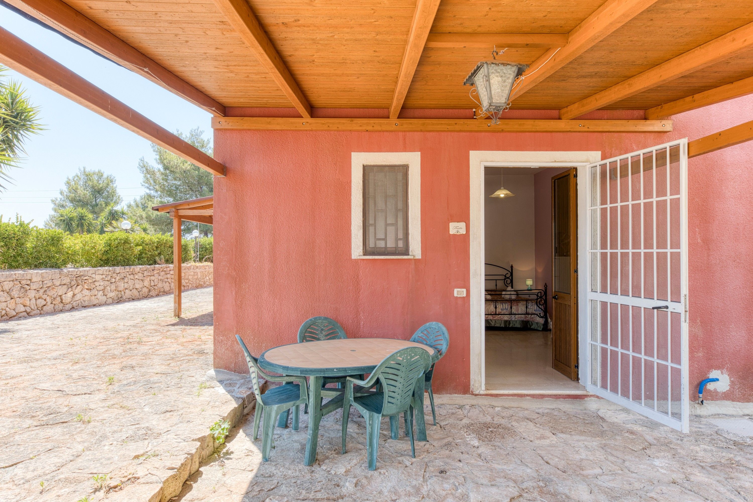 Portico esterno coperto con tavolo e sedie, soffitto in legno e vista su un giardino.