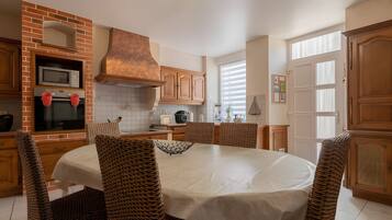 Een keuken met een tegelwand, houten keukenkastjes, een ronde eettafel met stoelen en een inbouwoven.
