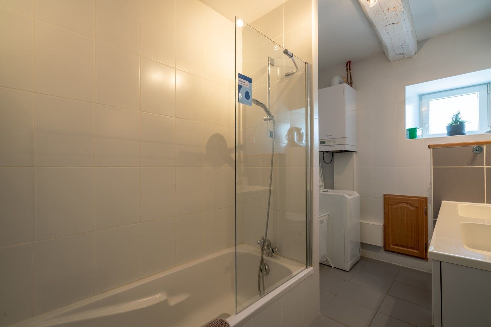 Ein modernes Badezimmer mit einer einachigen Duschkabine, einem weißen Waschbecken und einem Fenster für natürliches Licht.