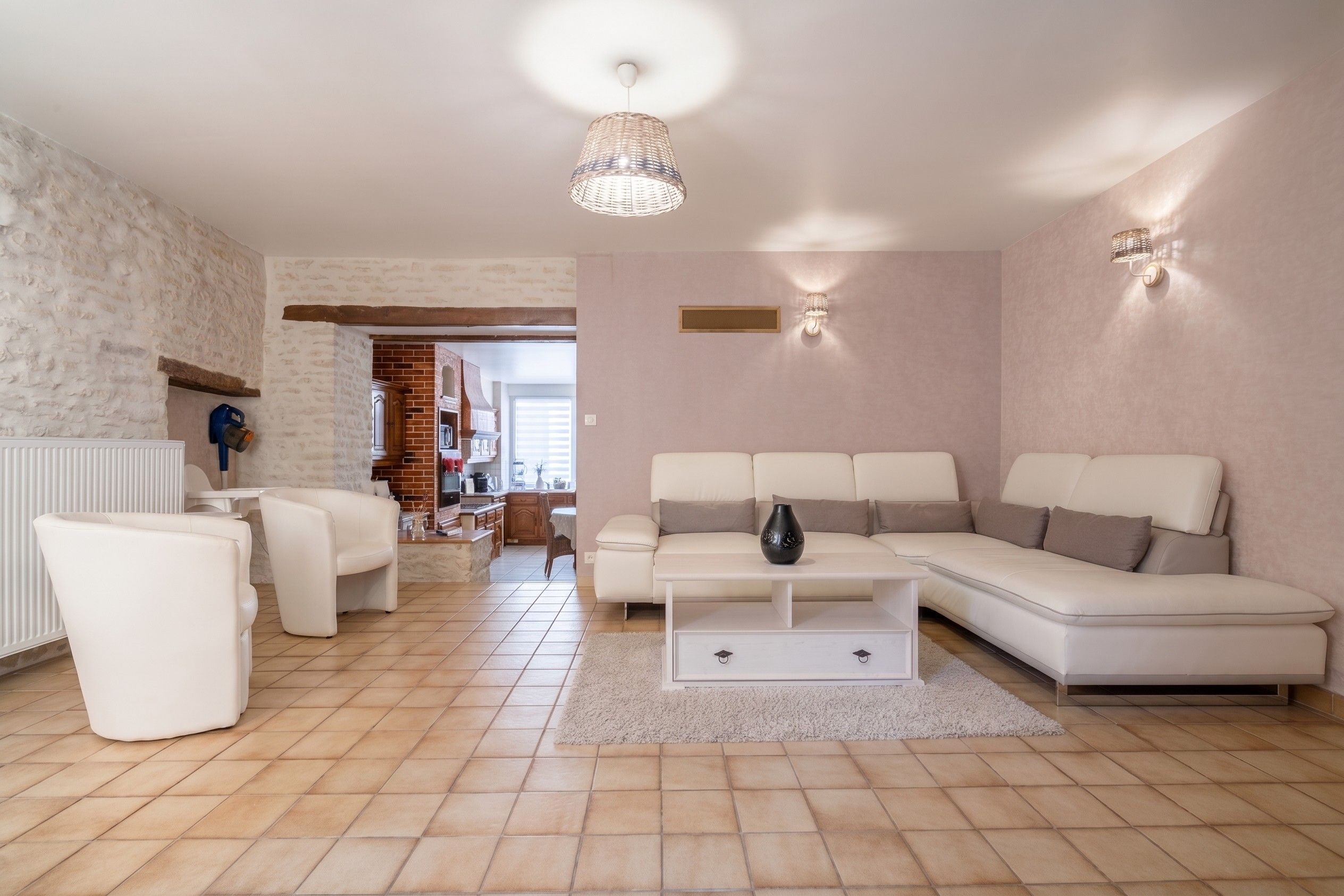 Un salon moderne avec un canapé d’angle, une table basse et un coin repas, la cuisine étant visible au fond.