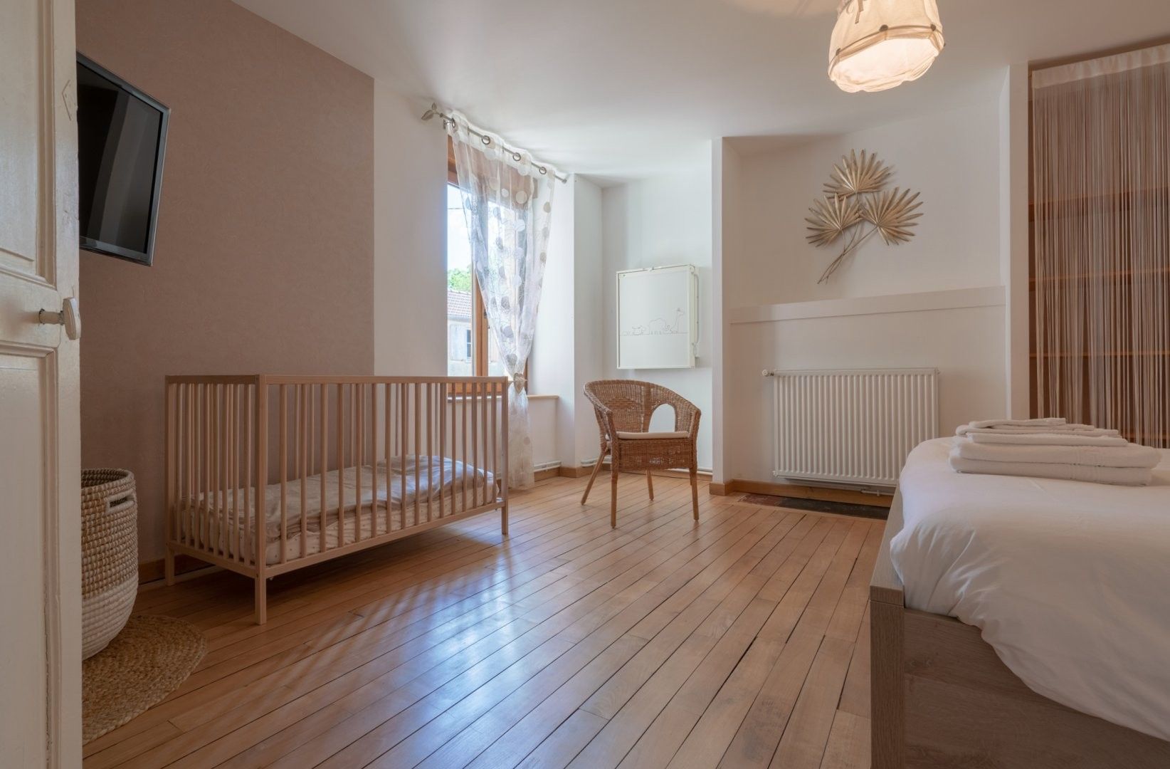 Een slaapkamer met een houten vloer, een ledikantje, een stoel, een bed met handdoeken, een radiator en een aan de muur bevestigde televisie.