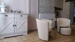 Un interior moderno con un armario blanco, dos sillas blancas, una mesita y un radiador.