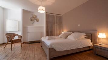 Ein Schlafzimmer mit einem Bett, einem Sessel, einem Nachttisch mit Lampe, einer Heizung und einer Wandleuchte.