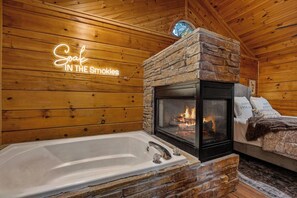A wooden cabin interior with a stone fireplace, a white bathtub, and a neon sign that reads 'Soak in the Smokles.' - The Dwell Cabin NEW LISTING DISCOUNT, Screened-In Hot Tub (Sevierville)