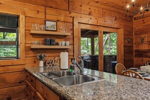 Ein Holzblockhaus-Interieur mit einer Granit-Arbeitsplatte, einem Edelstahl-Spülbecken und einem Essbereich mit Tisch und Stühlen.
