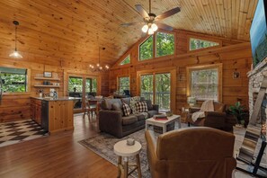 Ein geräumiges Blockhauskabinen-Interieur mit Holzbalkendecke, großen Fenstern, einem Essbereich und einer Küche.