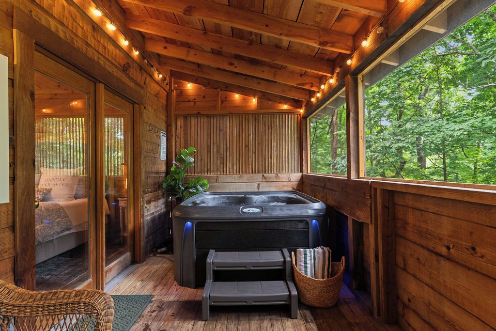 Interior de una cabaña de madera con jacuzzi, cama y vistas al bosque.