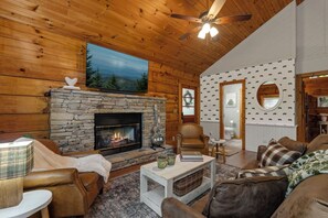 A cozy living room with a stone fireplace, leather furniture, and a large painting of a landscape. - The Dwell Cabin NEW LISTING DISCOUNT, Screened-In Hot Tub (Sevierville)