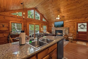 A log cabin interior with a kitchen, dining area, fireplace, and large windows. - The Dwell Cabin NEW LISTING DISCOUNT, Screened-In Hot Tub (Sevierville)
