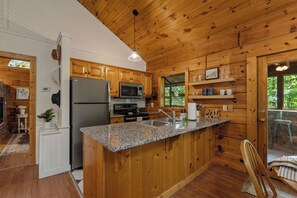 A wooden cabin kitchen with a granite countertop, stainless steel appliances, and a view of the outdoors. - The Dwell Cabin NEW LISTING DISCOUNT, Screened-In Hot Tub (Sevierville)
