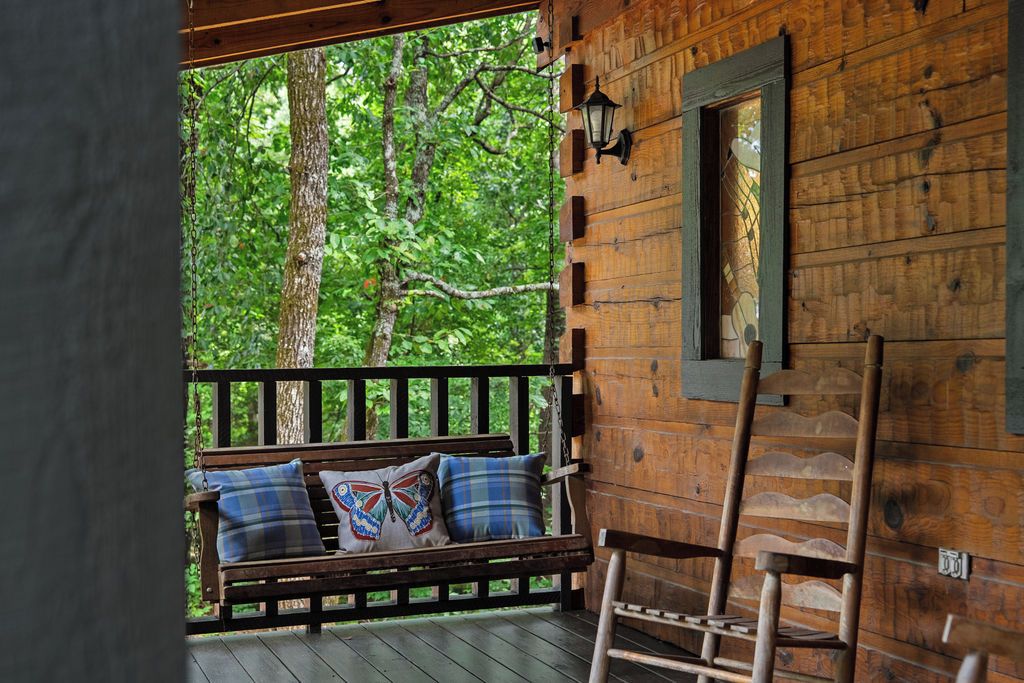 A wooden cabin with a porch, a bench with pillows, and a ladder.