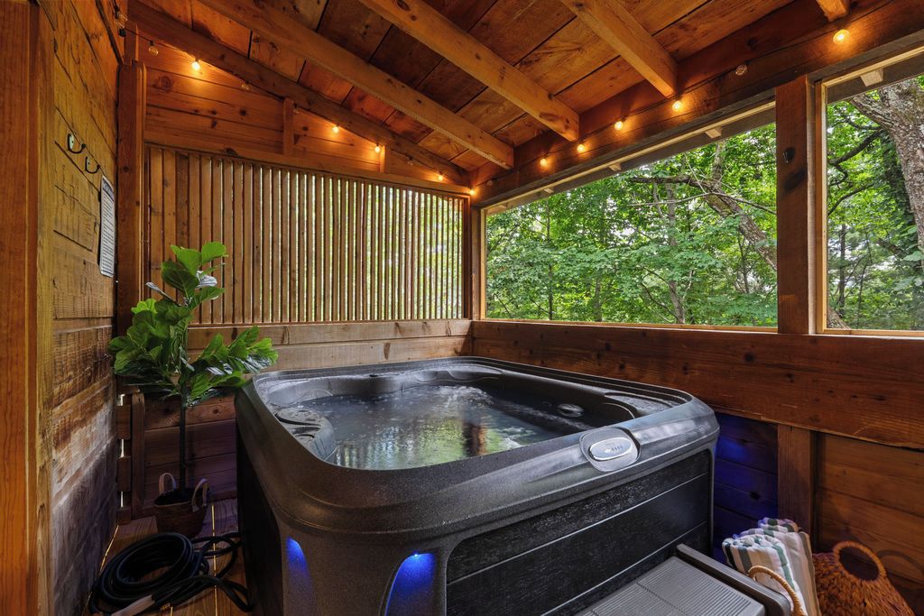 A wooden cabin with a hot tub, a window with a view of trees, and a plant.