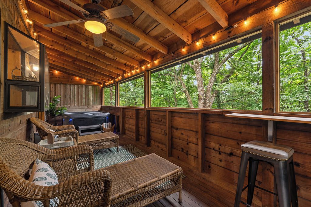 A wooden deck with wicker furniture, a bar stool, and a grill.