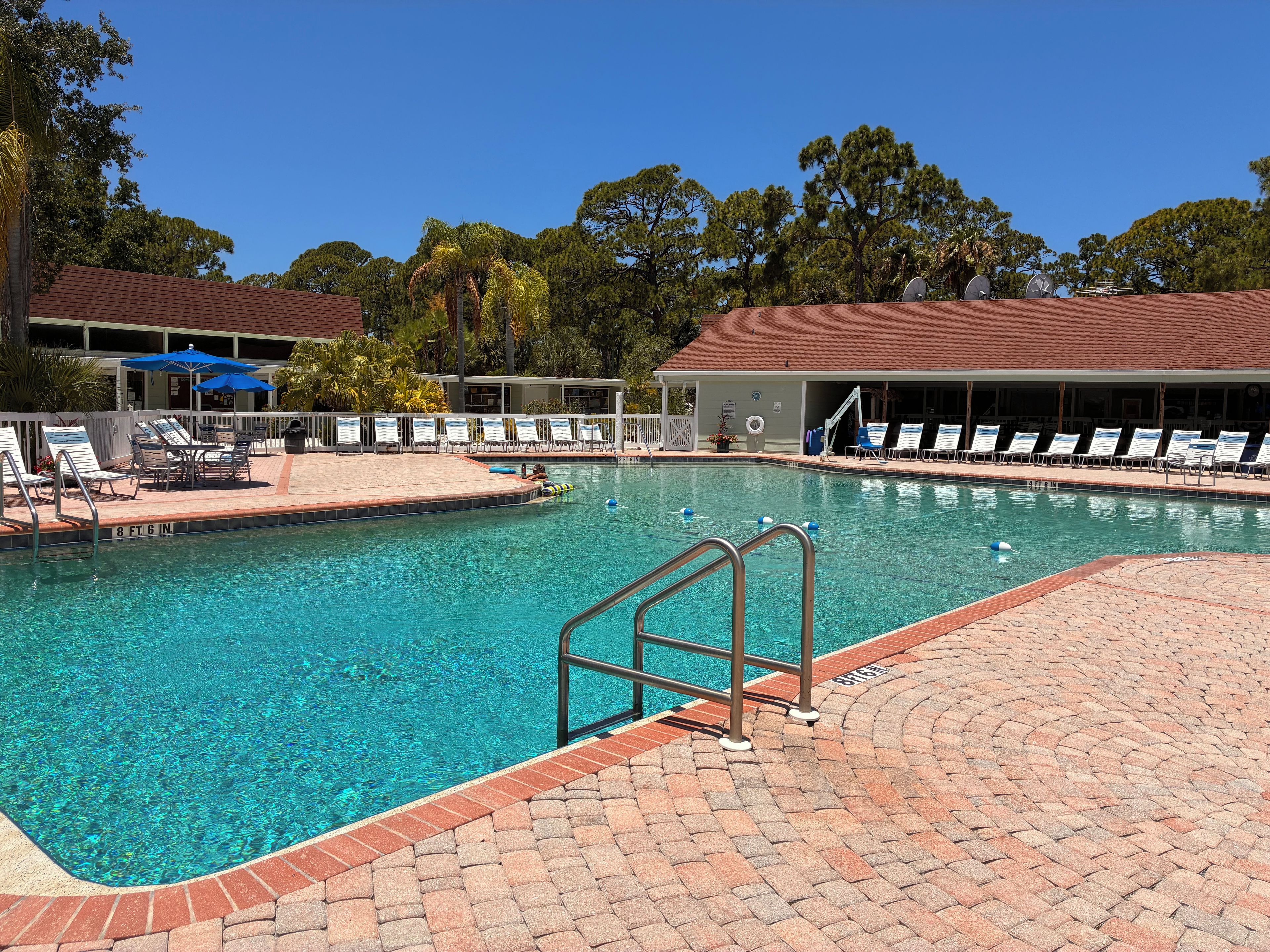 Ein Schwimmbecken mit einer Ziegelterrasse, Liegestühlen und Sonnenschirmen.