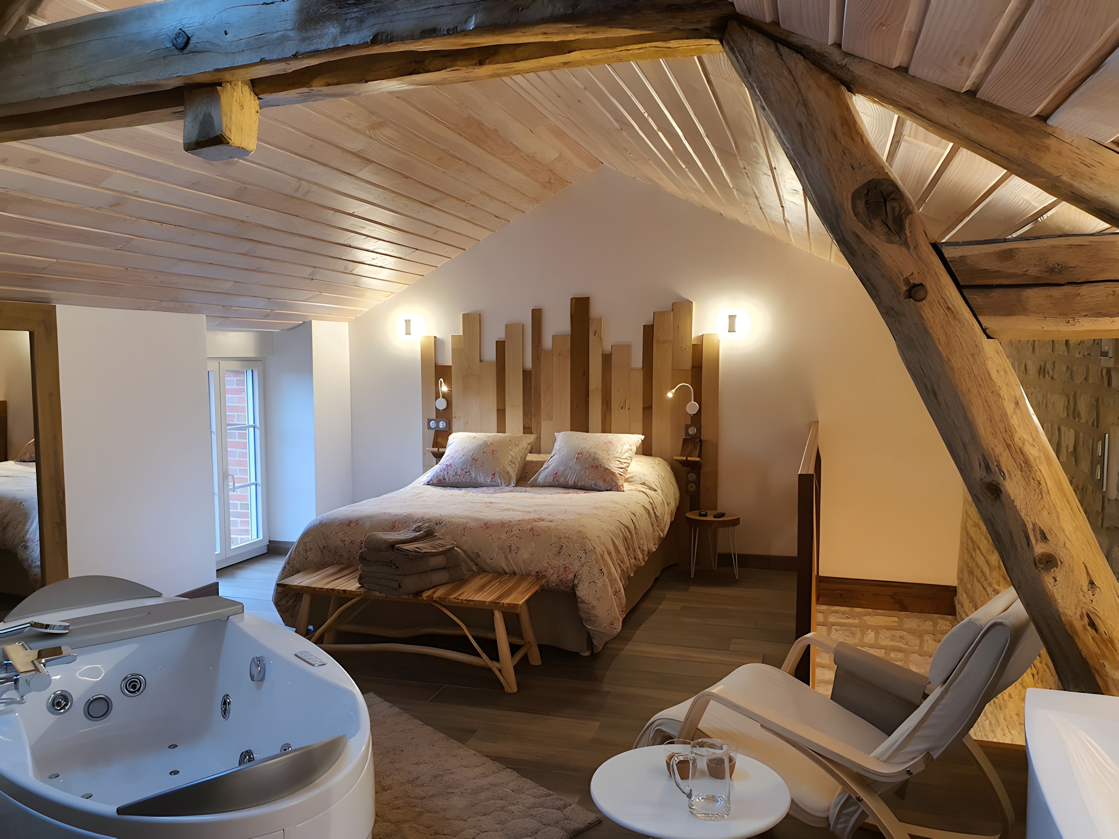 Un dormitorio con techo inclinado, una cama grande, una bañera y un sillón.