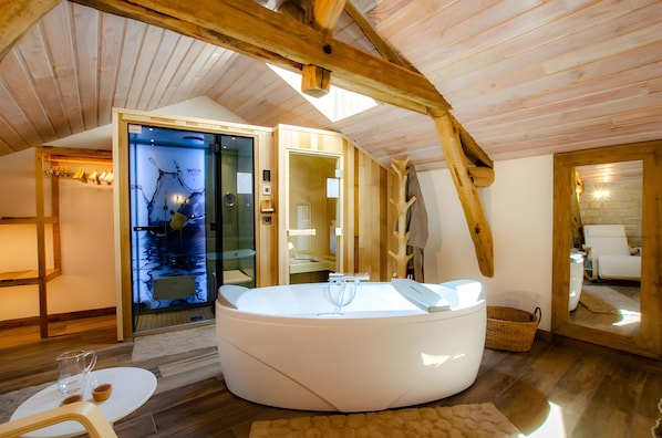 A modern bathroom with a large bathtub, wooden beams, and a glass door leading to a shower area.