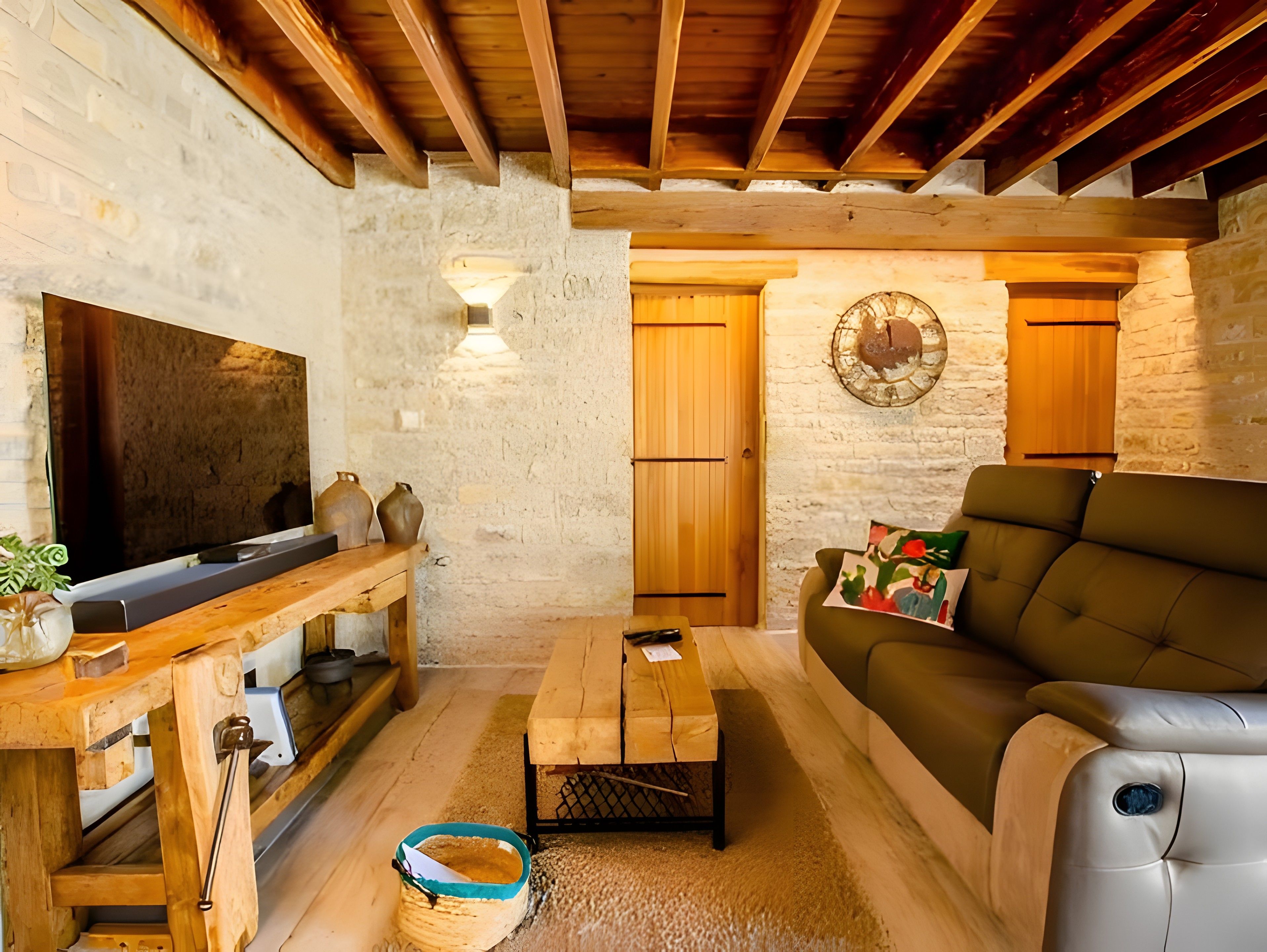 Un salon chaleureux avec un plafond en bois, un téléviseur à écran plat, une table basse en bois, un canapé et un mur en pierre.