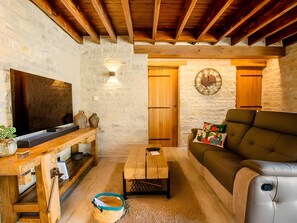 Un saló d'estar acollidor amb sostre de fusta, un televisió de pantalla plana, una taula de centre de fusta, un sofà i una paret de pedra.