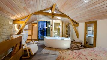 Ein gemütliches Schlafzimmer mit schrägen Wänden, einem großen Bett, einer Sitzecke mit Stuhl und Tisch sowie einem Badezimmer mit Badewanne.