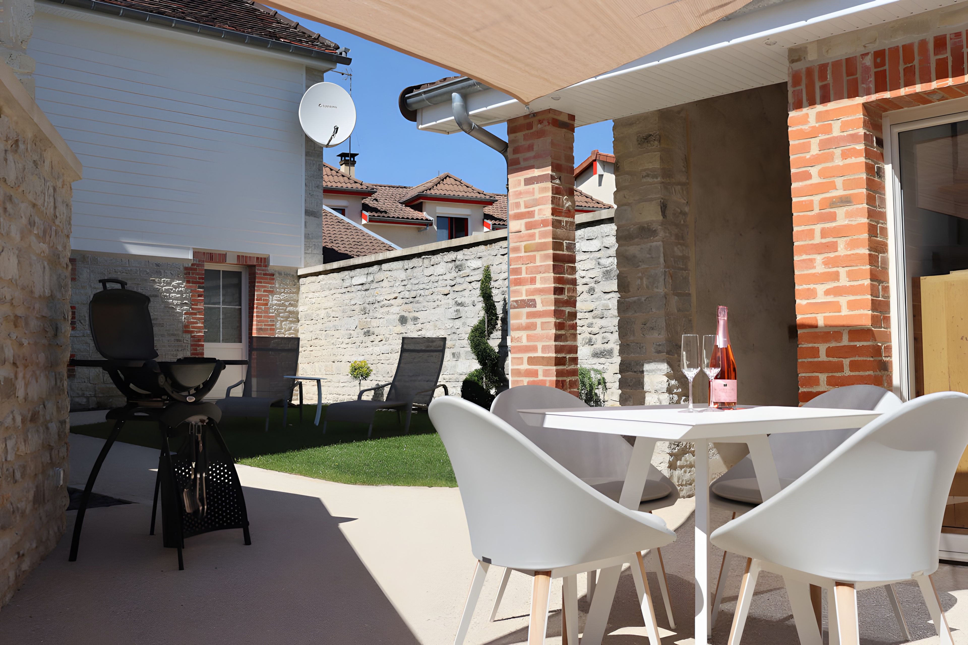 Une terrasse extérieure avec une table et des chaises, un barbecue et une bouteille de vin.