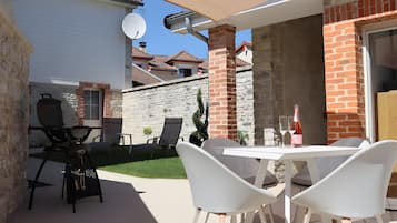 Une terrasse extérieure avec une table et des chaises, un barbecue et une bouteille de vin.