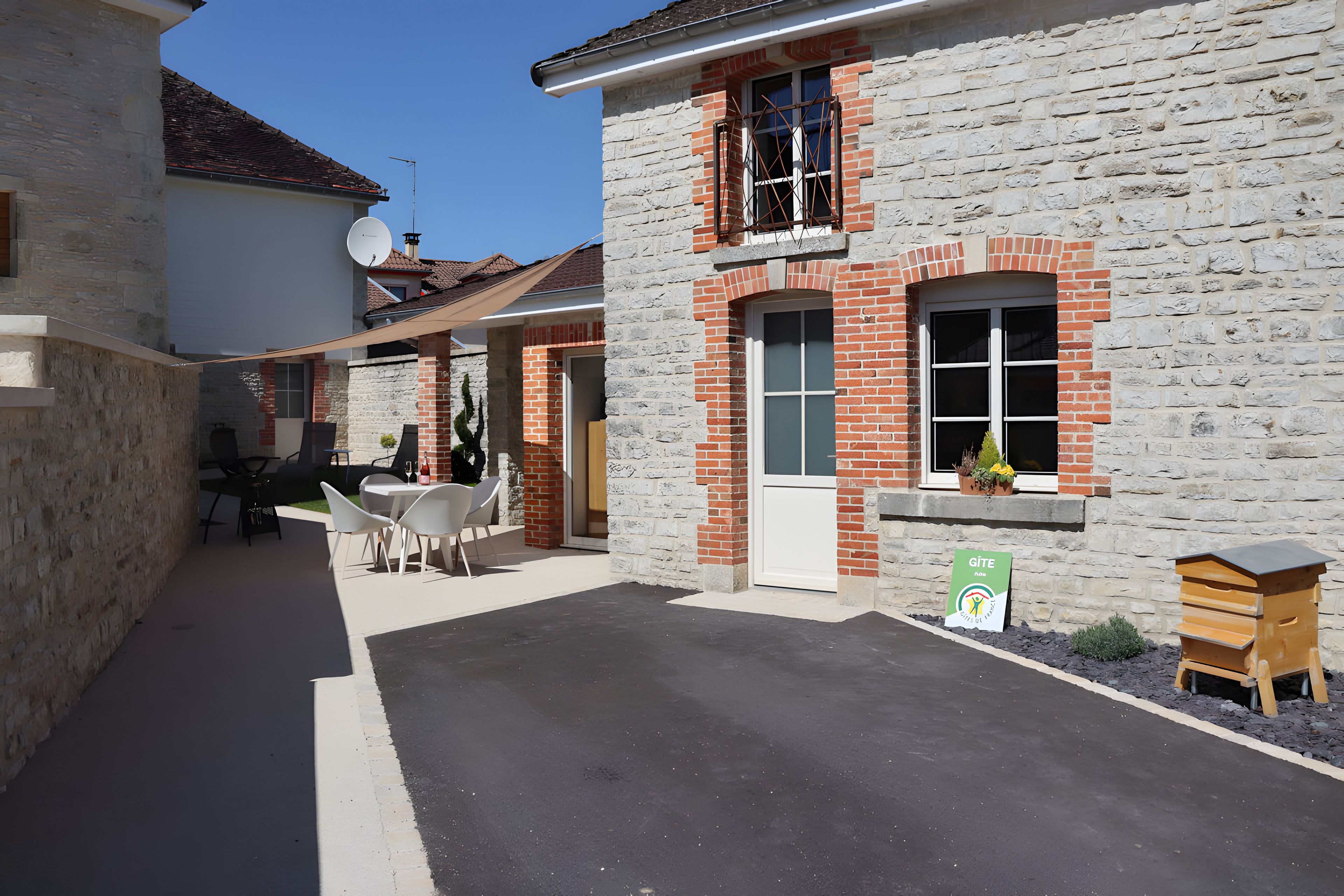 Une ruelle bordée de bâtiments en pierre, une table avec des chaises et une ruche.