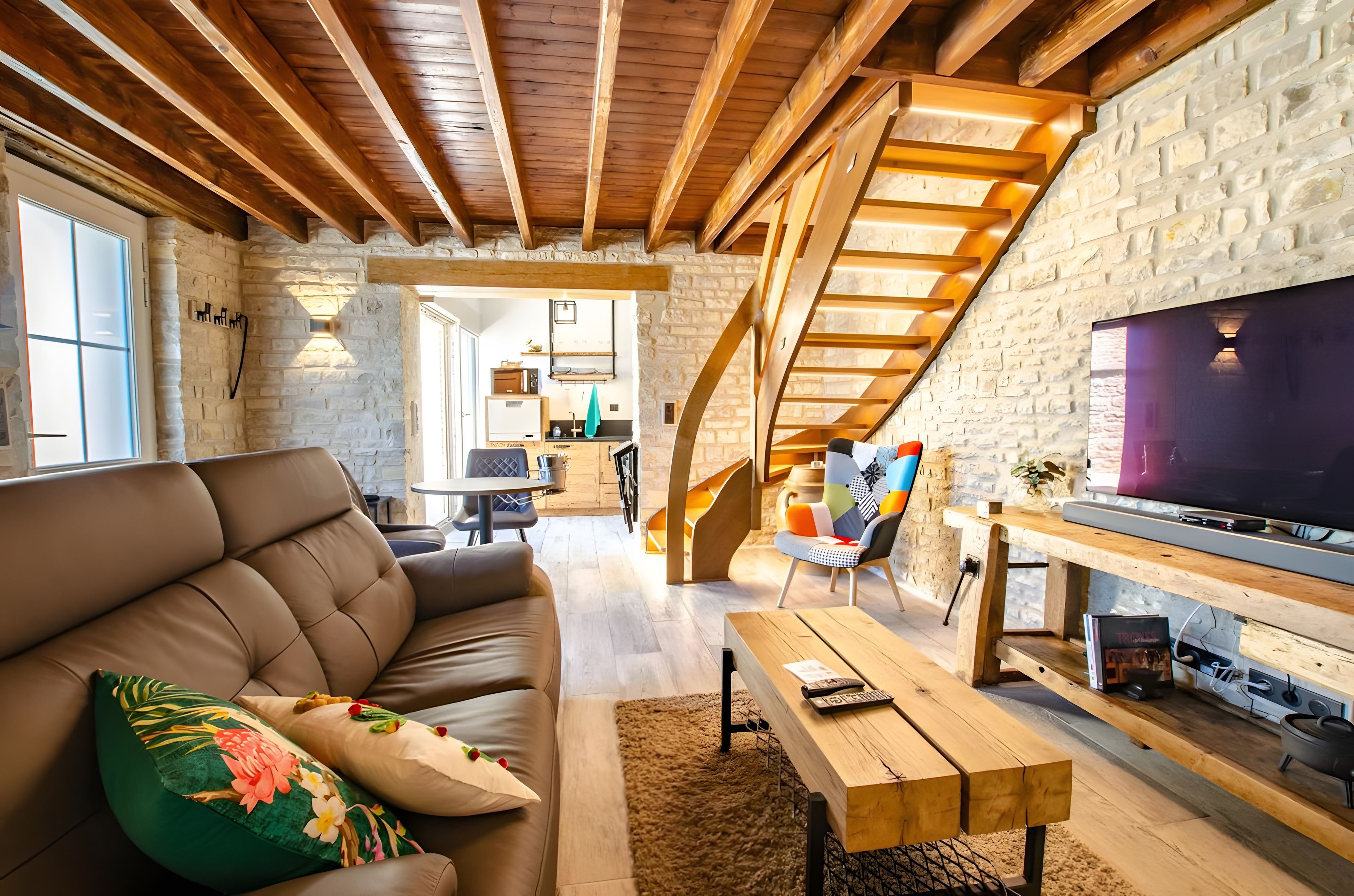 A modern living room with a sofa, a coffee table, and a TV. There is a staircase leading to an upper level.