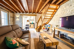 A modern living room with a sofa, a coffee table, and a TV. There is a staircase leading to an upper level.
