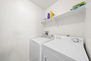 A laundry room with two white washing machines and a shelf above containing cleaning supplies. - Azure Horizon - 3 BR Ocean Views & Resort Pool (Marina del Rey)