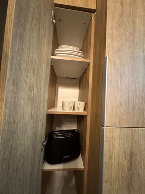 A wooden cabinet with shelves containing white cups, a black bag, and stacked plates. - Modern Apartment - 2 Bedrooms, 2 Bathrooms, and Parking (Santiago)