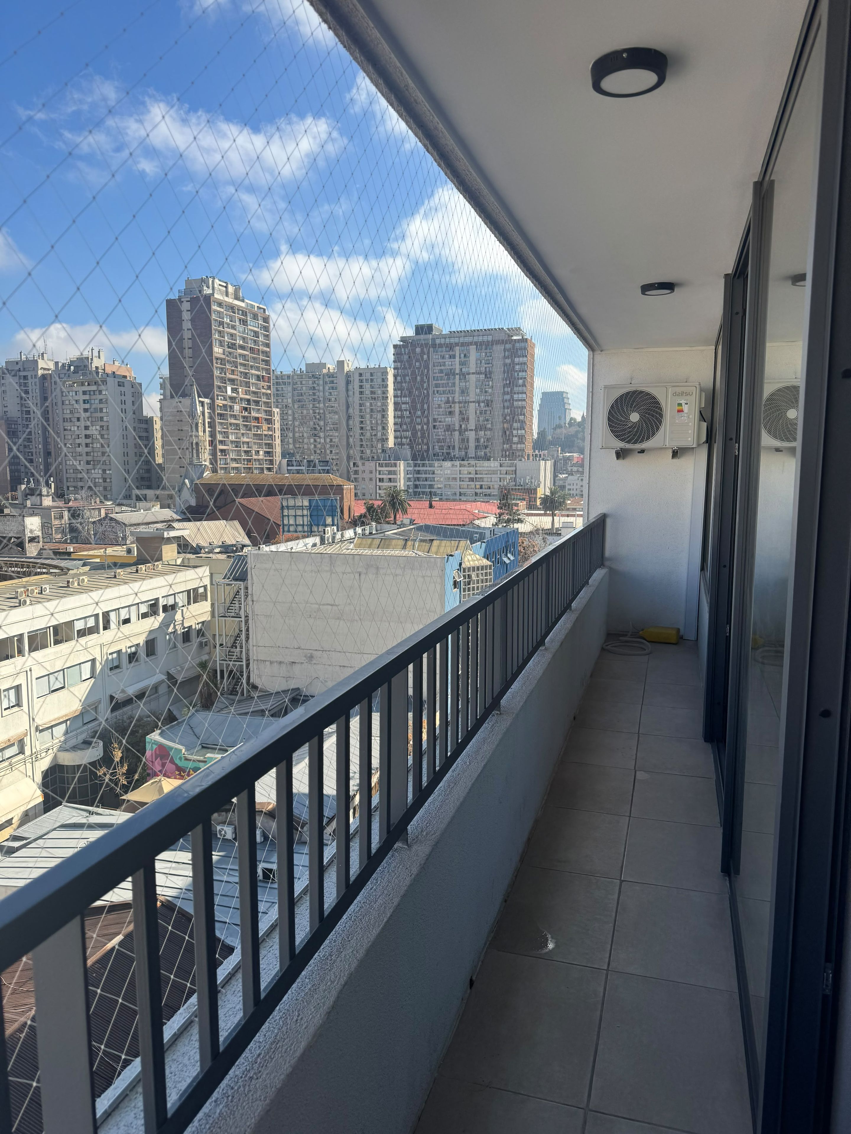 Un balcon offrant une vue sur le paysage urbain, avec de hauts immeubles et un bâtiment dont le toit est rouge.