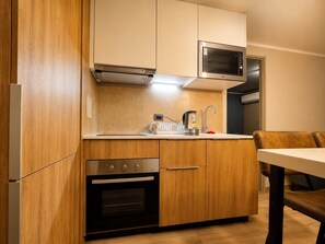 A compact kitchen with wooden cabinets, a built-in oven, a microwave, and a coffee maker. - Modern Apartment - 2 Bedrooms, 2 Bathrooms, and Parking (Santiago)