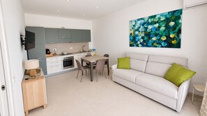 A modern kitchen with grey cabinets, a dining table with chairs, a white sofa with green cushions, and a painting on the wall. - Beachfront villa with a garden and private parking on the property. (Avola)