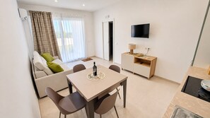 A modern living room with a sofa, a dining table with chairs, a television, and a kitchen area with a microwave. - Beachfront villa with a garden and private parking on the property. (Avola)